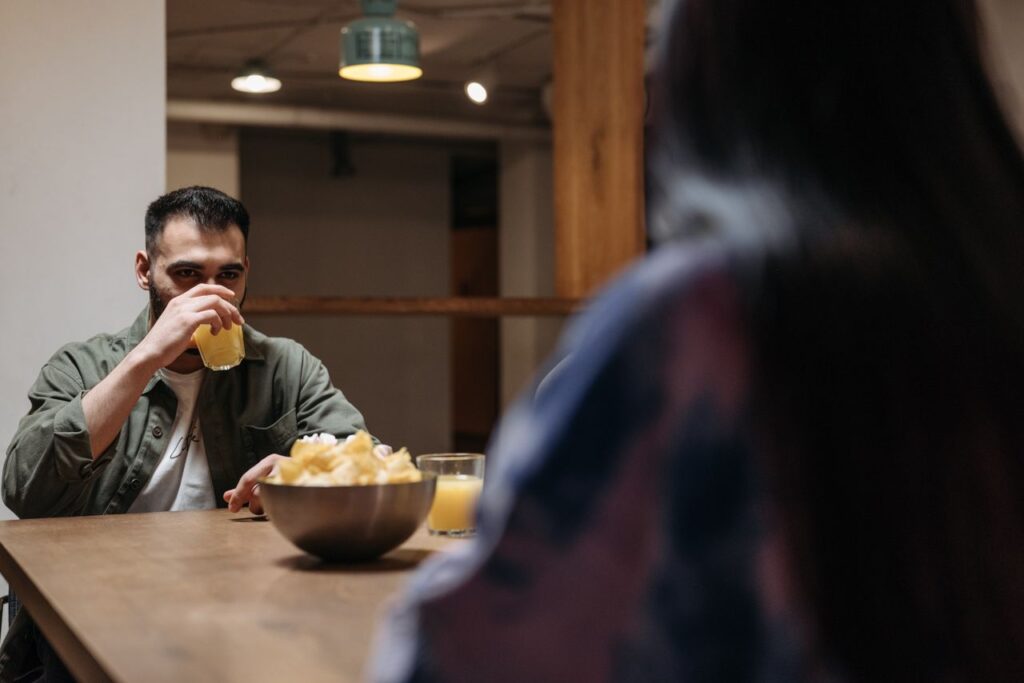 A man enjoys a refreshing drink indoors with a bowl of snacks on the wooden table.